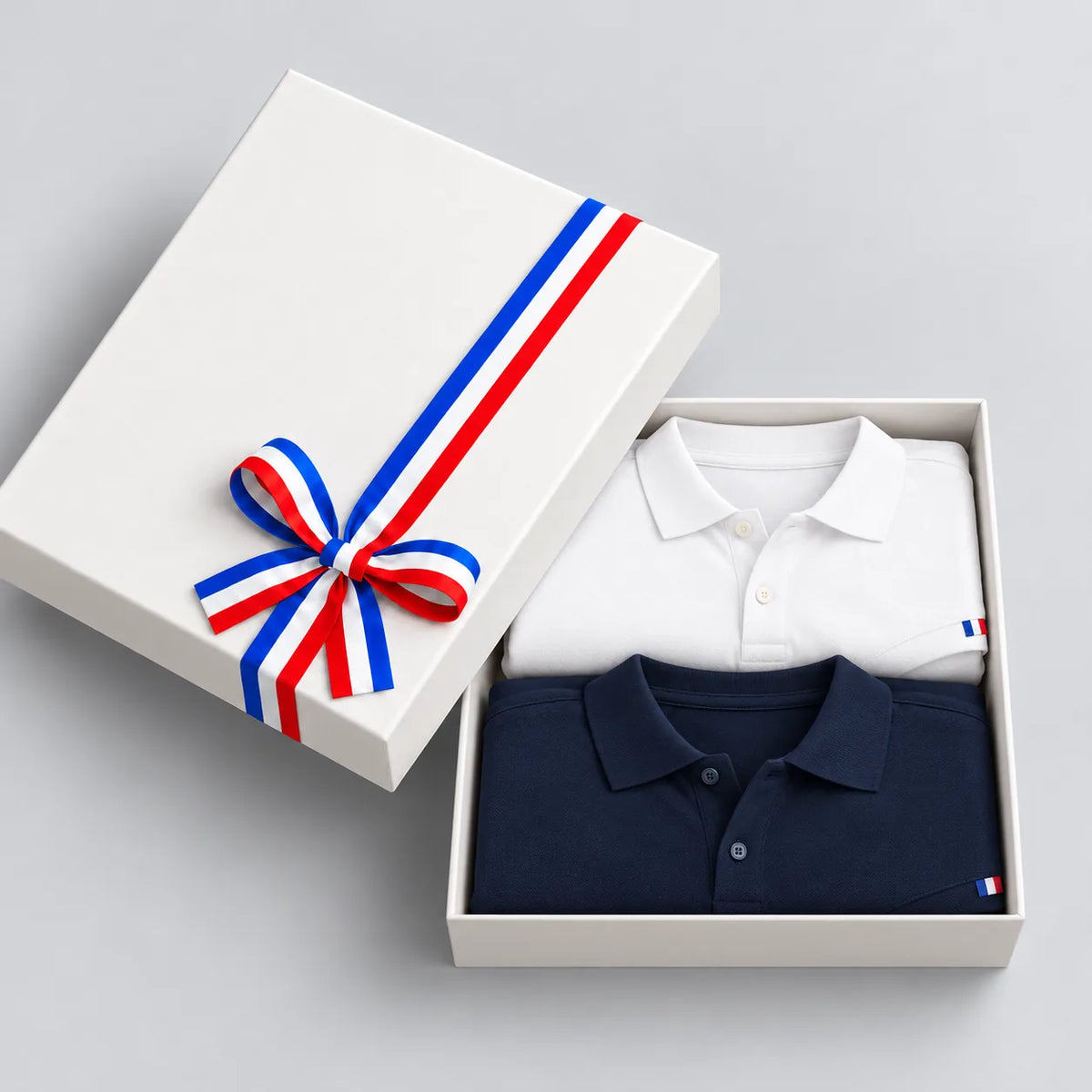 Coffret cadeau ouvert avec 2 polos homme en coton bio, bleu marine et blanc, couvercle à ruban tricolore