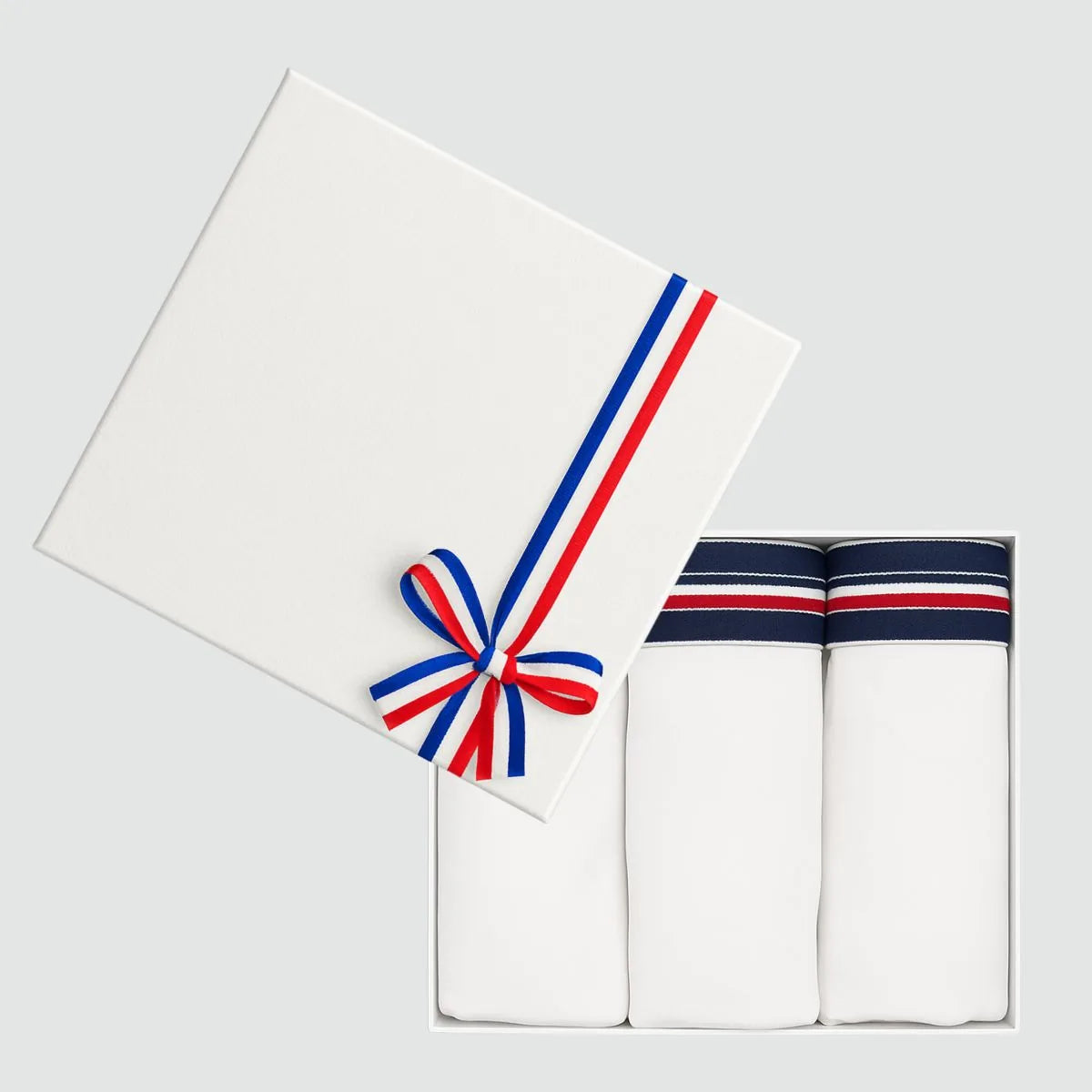Coffret cadeau ouvert avec 3 slips homme blancs en coton bio, couvercle blanc à ruban tricolore