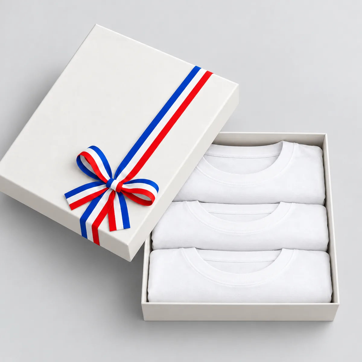 Coffret cadeau ouvert avec 3 t-shirts homme blancs col rond pliés, couvercle à ruban tricolore