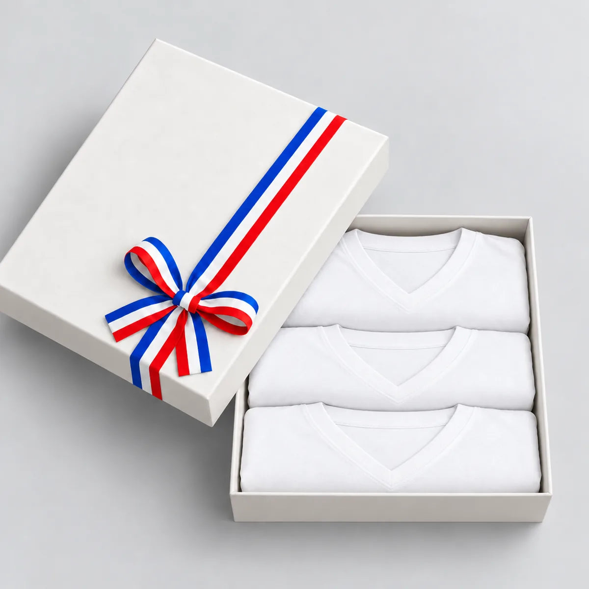 Coffret cadeau ouvert avec 3 t-shirts homme blancs col V pliés, couvercle à ruban tricolore