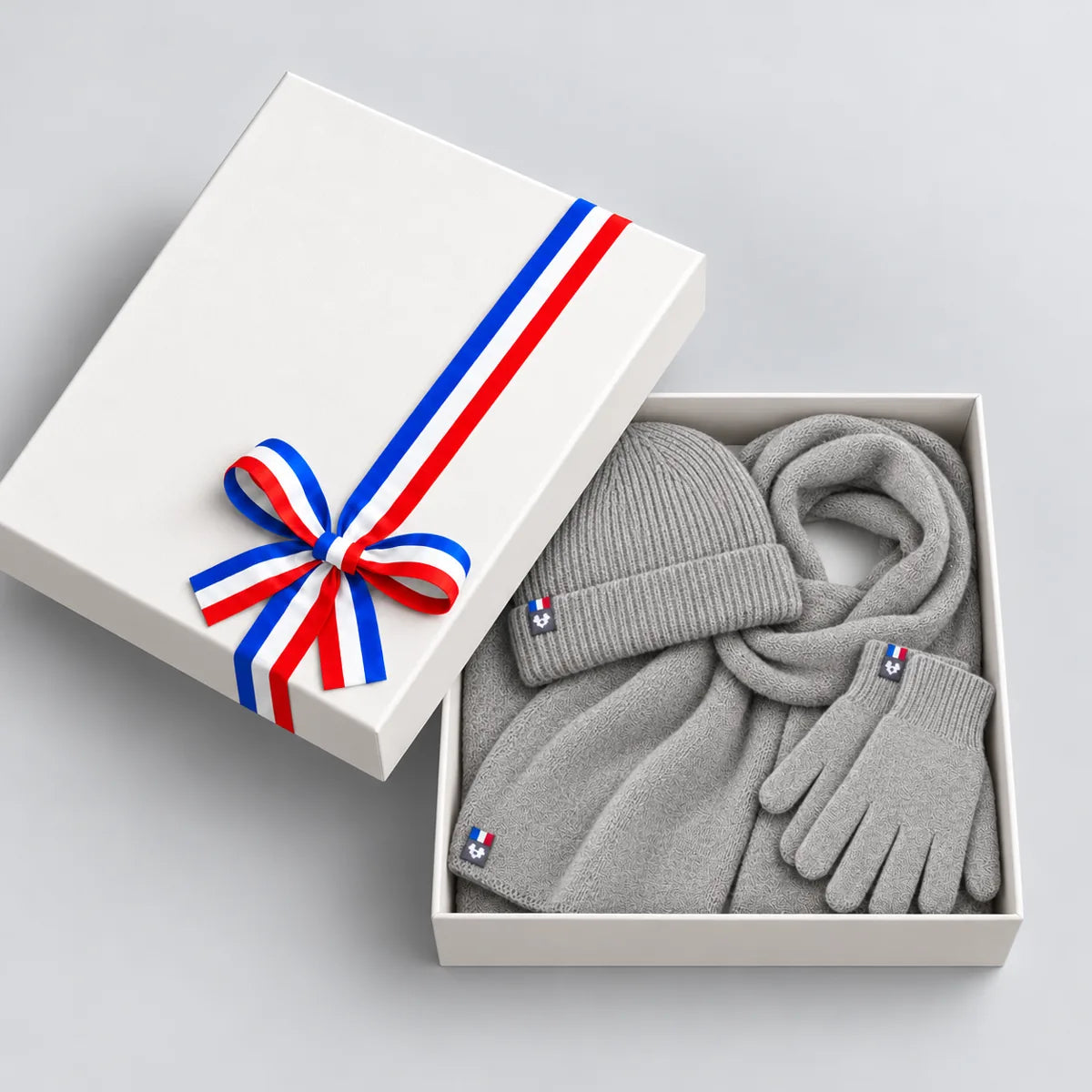 Coffret cadeau ouvert avec écharpe, bonnet et gants gris en laine mérinos, couvercle à ruban tricolore