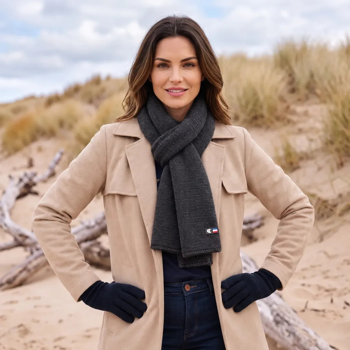 Femme en manteau beige portant l'écharpe en cachemire noire nouée, dans les dunes