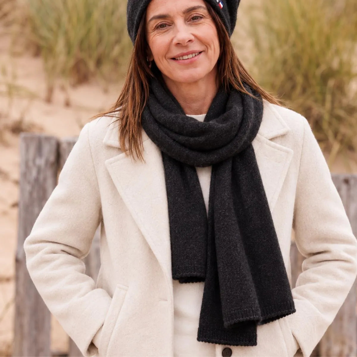 Femme en manteau blanc portant l'écharpe en cachemire noire et le bonnet assorti
