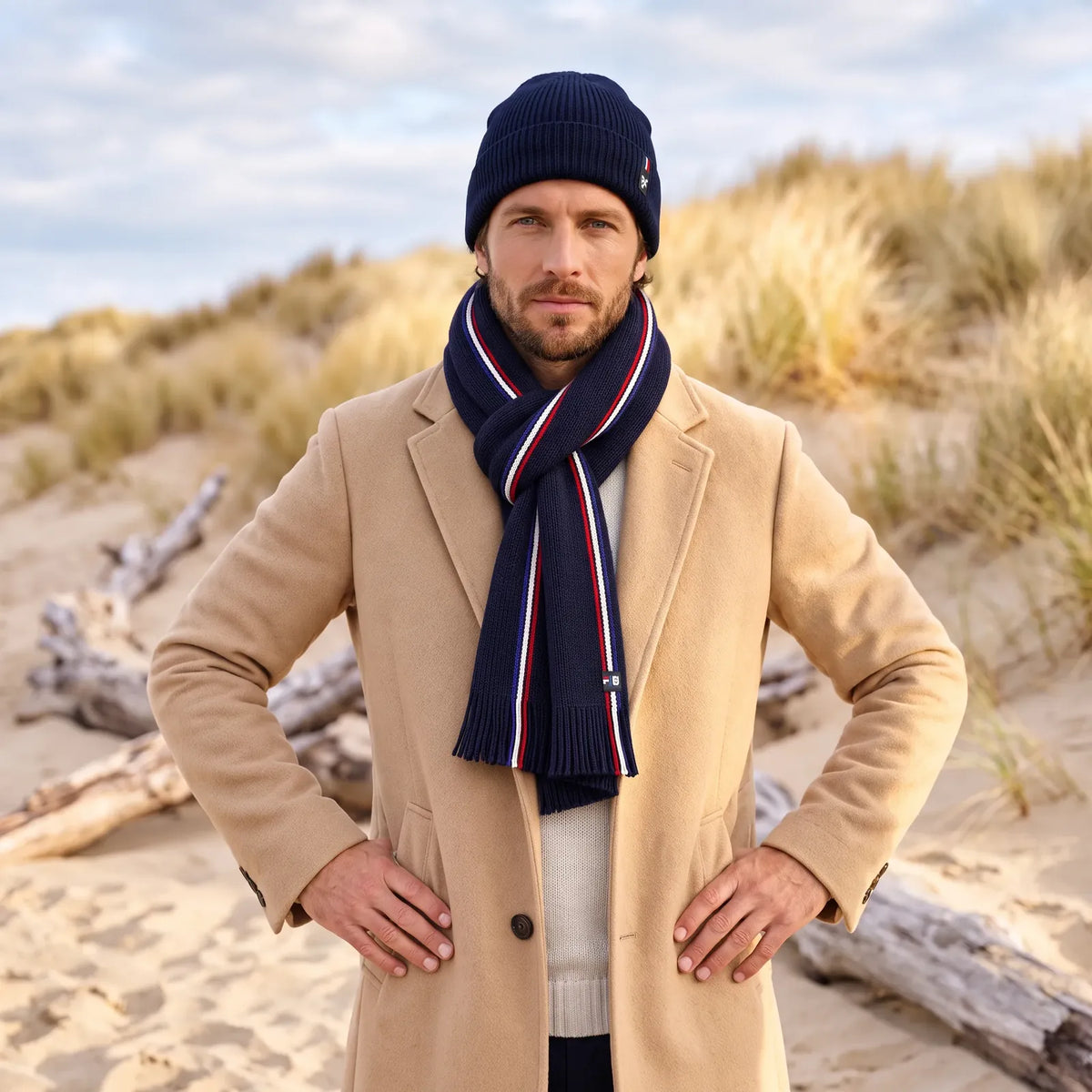 Homme en manteau camel et pull écru portant l'écharpe tricolore bleu marine nouée et un bonnet bleu marine
