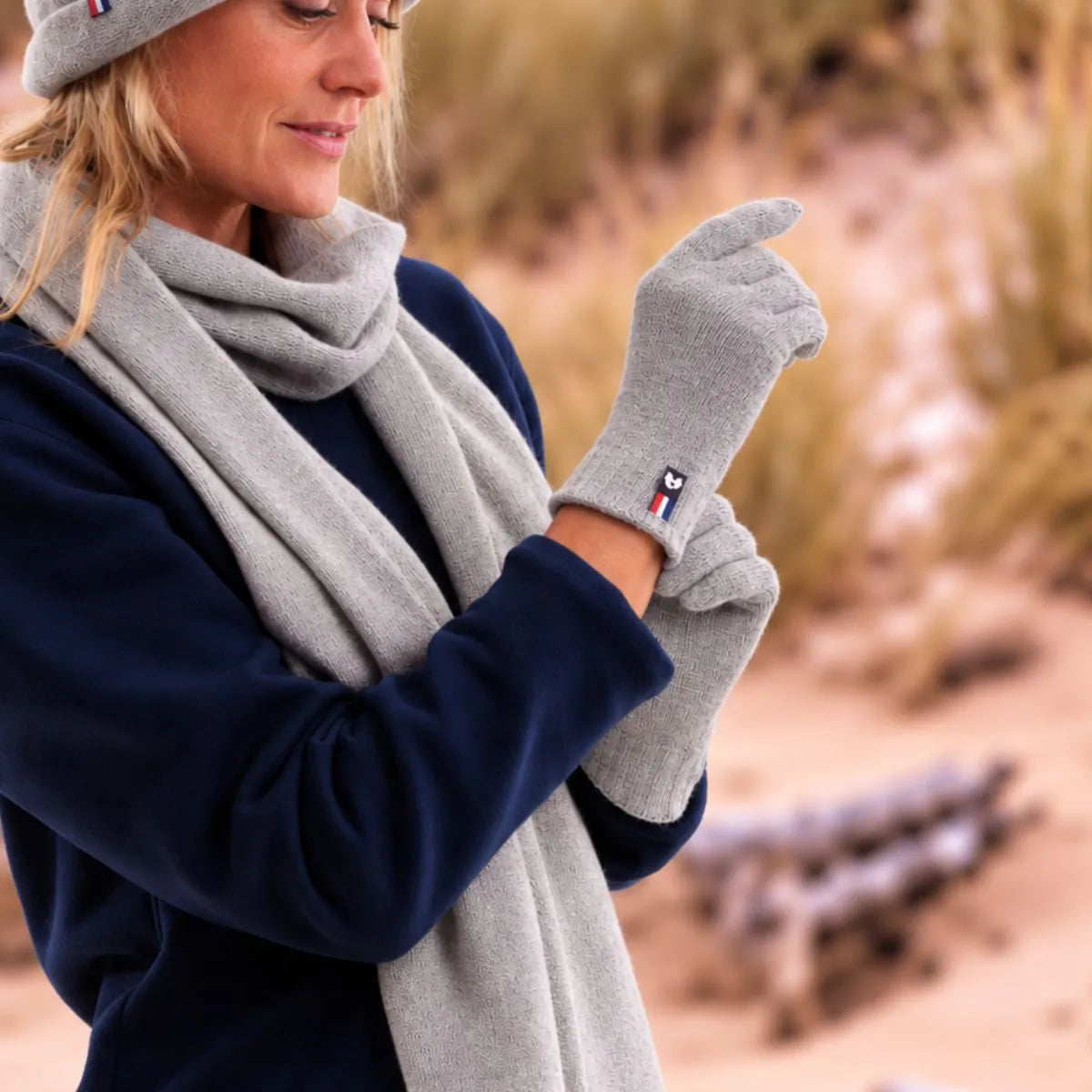 Femme enfilant les gants tactiles en cachemire gris, avec l'écharpe et le bonnet assortis