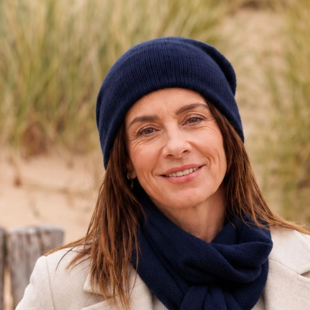 Femme souriante en manteau crème portant le bonnet en cachemire bleu marine et l'écharpe assortie