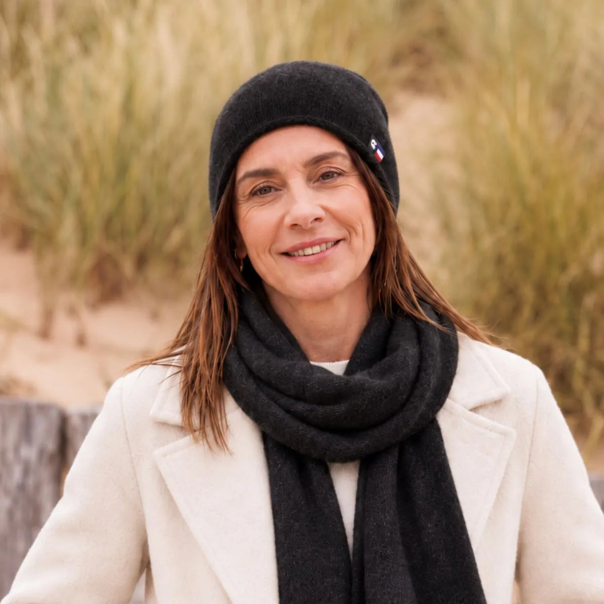 Femme souriante en manteau blanc portant le bonnet en cachemire noir et l'écharpe assortie