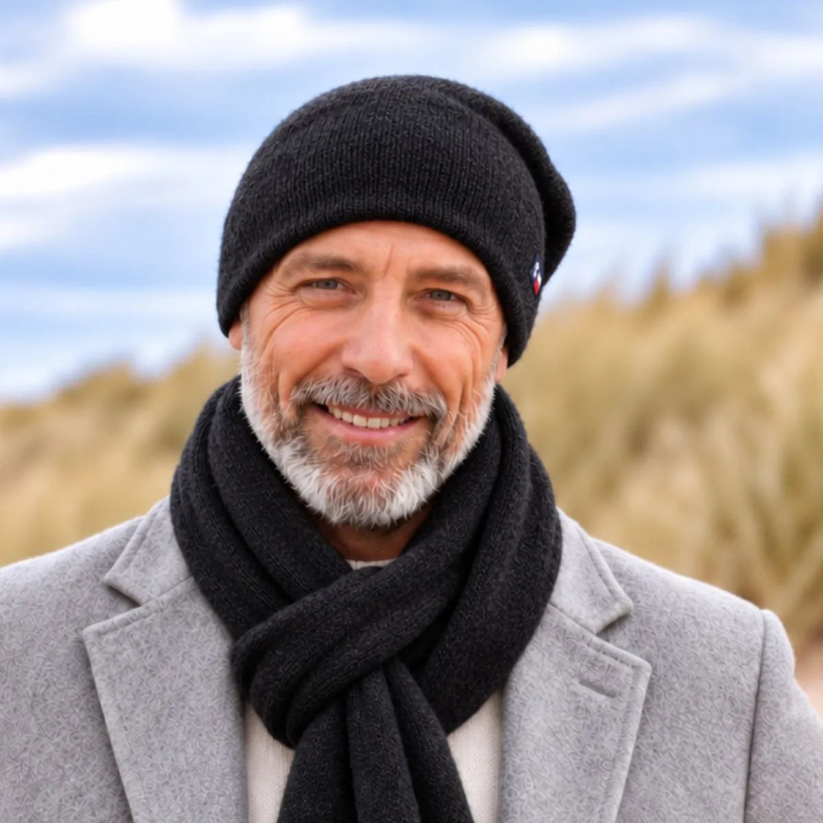 Homme barbu en manteau gris portant le bonnet et l'écharpe en cachemire noirs, dans les dunes