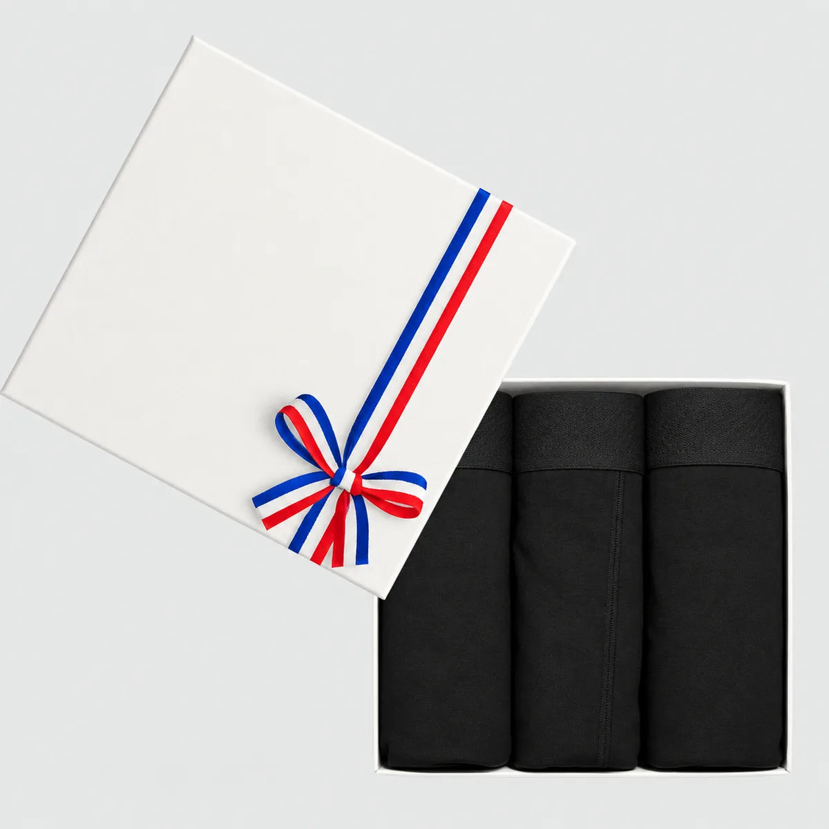Coffret cadeau blanc ouvert avec 3 boxers homme noirs en coton bio, couvercle noué d'un ruban tricolore