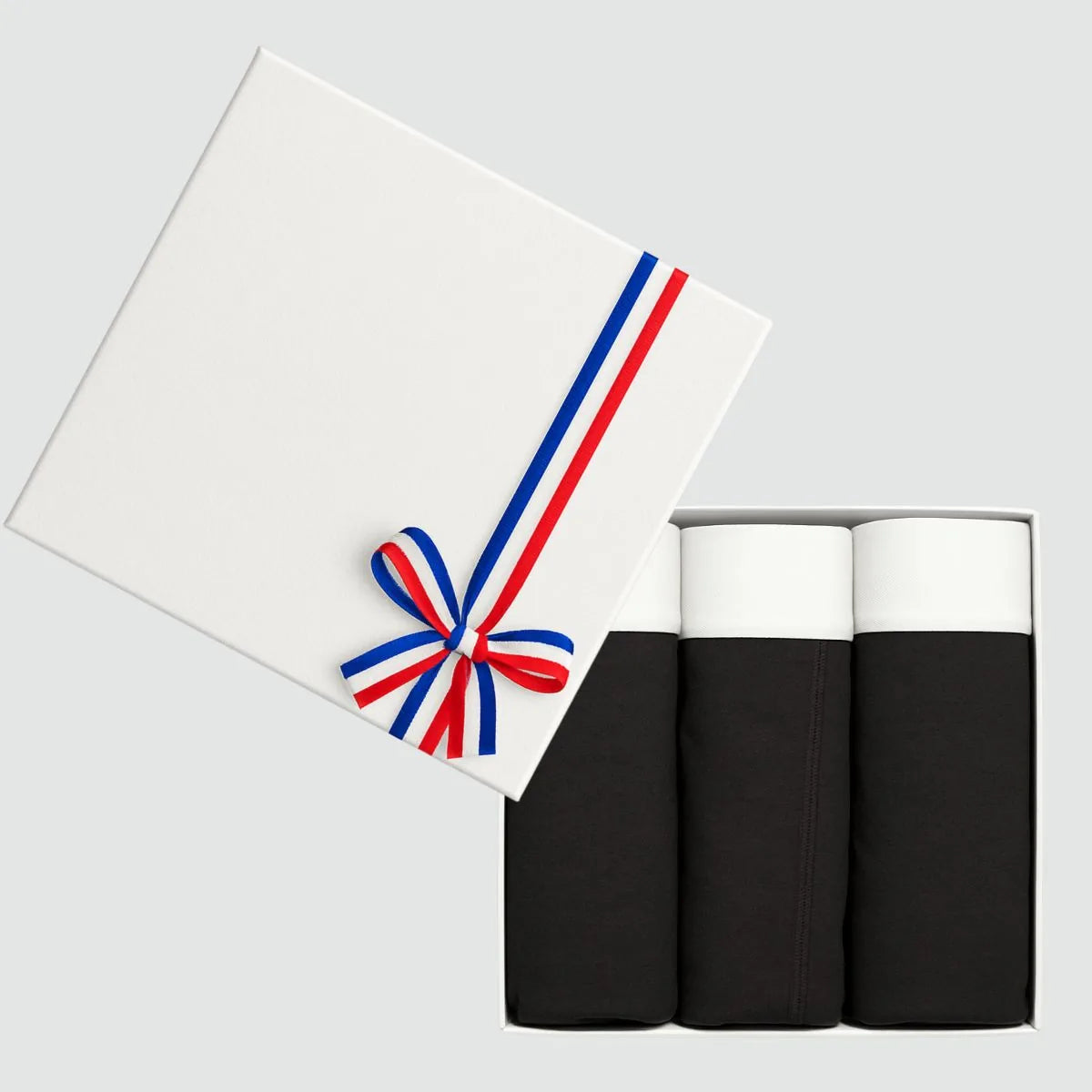 Coffret cadeau ouvert avec 3 slips homme noirs en coton bio à ceinture blanche, couvercle blanc à ruban tricolore