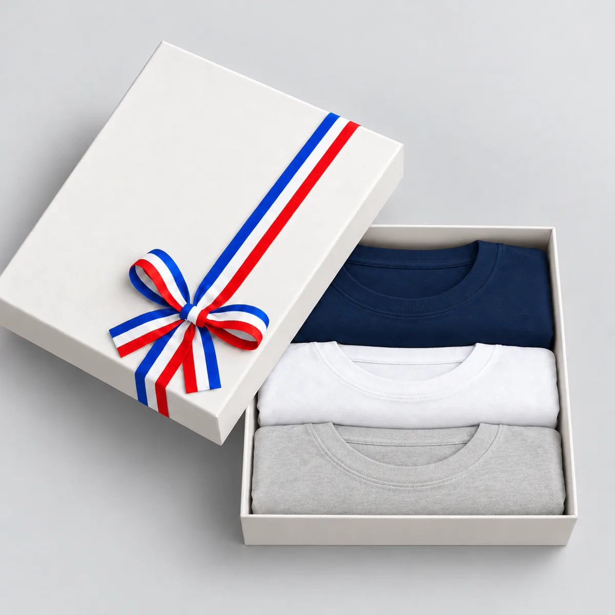Coffret cadeau ouvert avec 3 t-shirts homme col rond bleu marine, blanc et gris chiné, couvercle à ruban tricolore