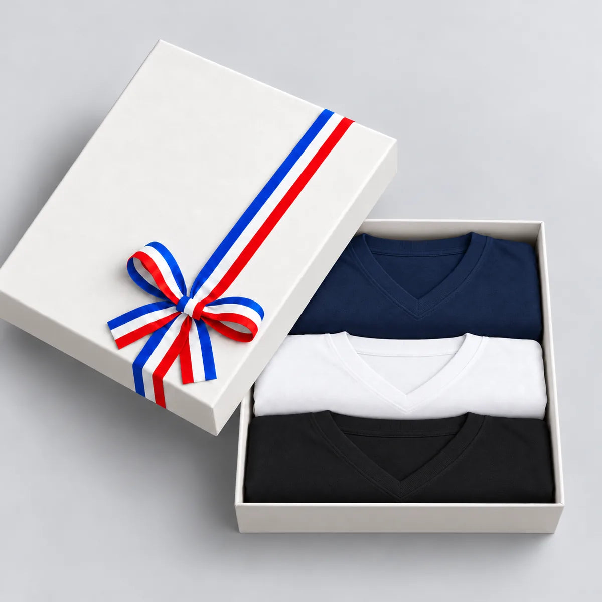 Coffret cadeau ouvert avec 3 t-shirts homme col V bleu marine, blanc et noir, couvercle à ruban tricolore