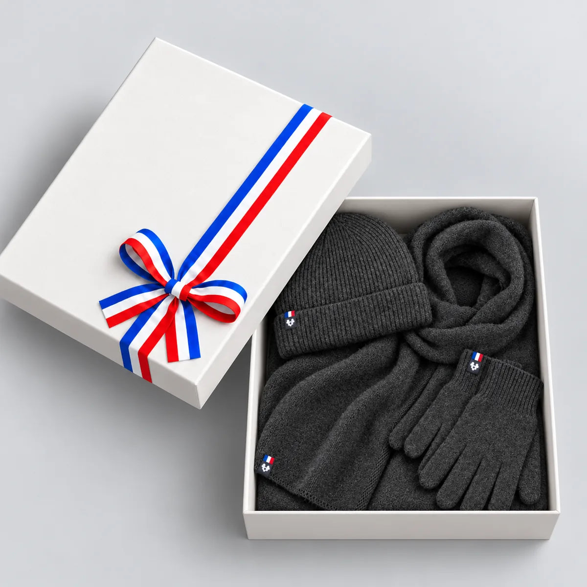 Coffret cadeau ouvert avec écharpe, bonnet et gants anthracite en laine mérinos, couvercle à ruban tricolore