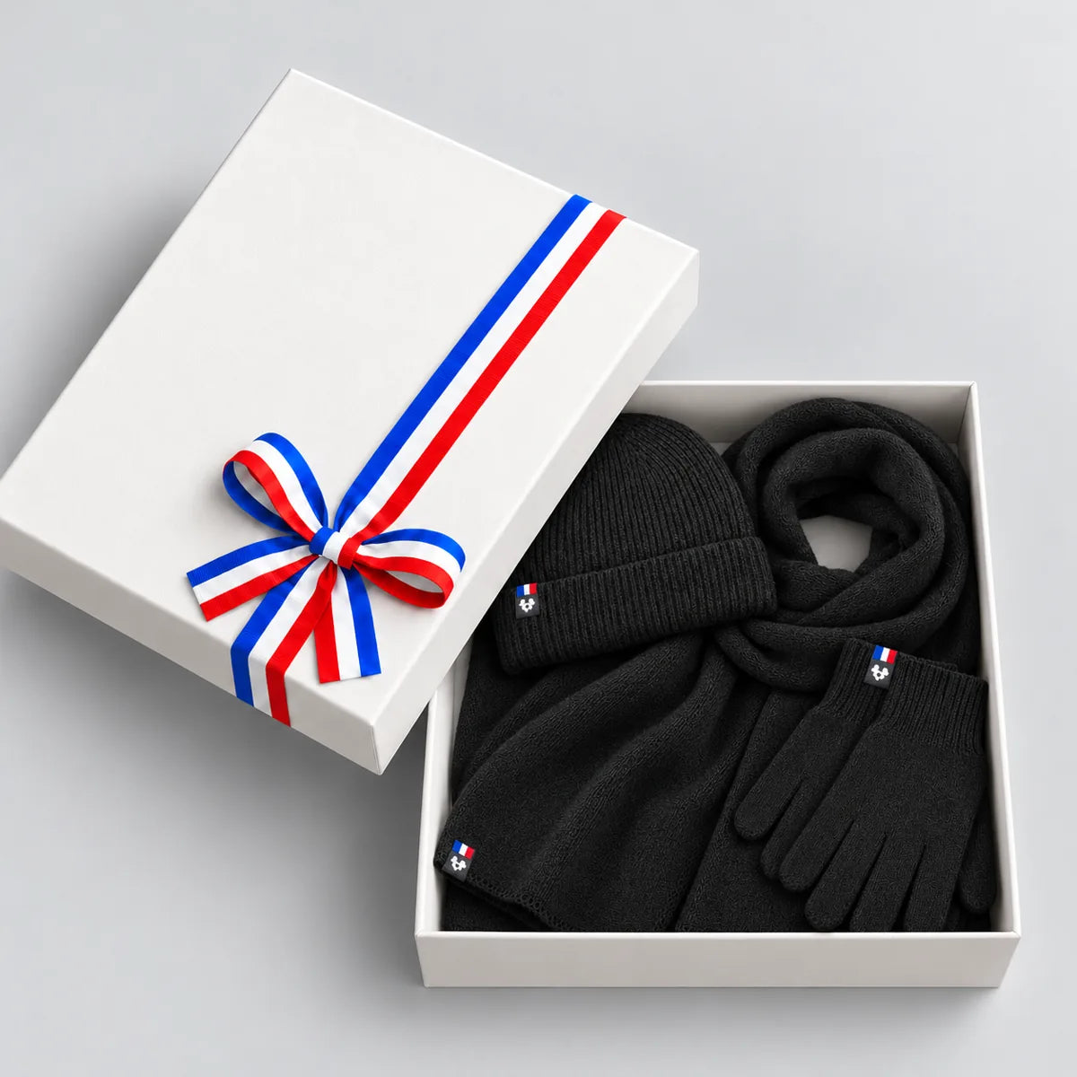 Coffret cadeau ouvert avec écharpe, bonnet et gants noirs en laine mérinos, couvercle à ruban tricolore