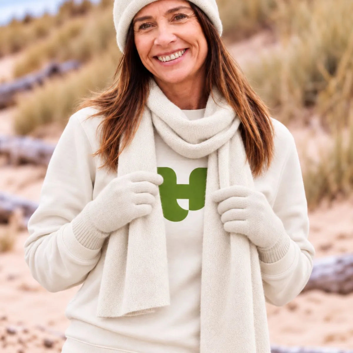 Femme dans les dunes portant l'écharpe en cachemire blanc cassé, le bonnet et les gants assortis