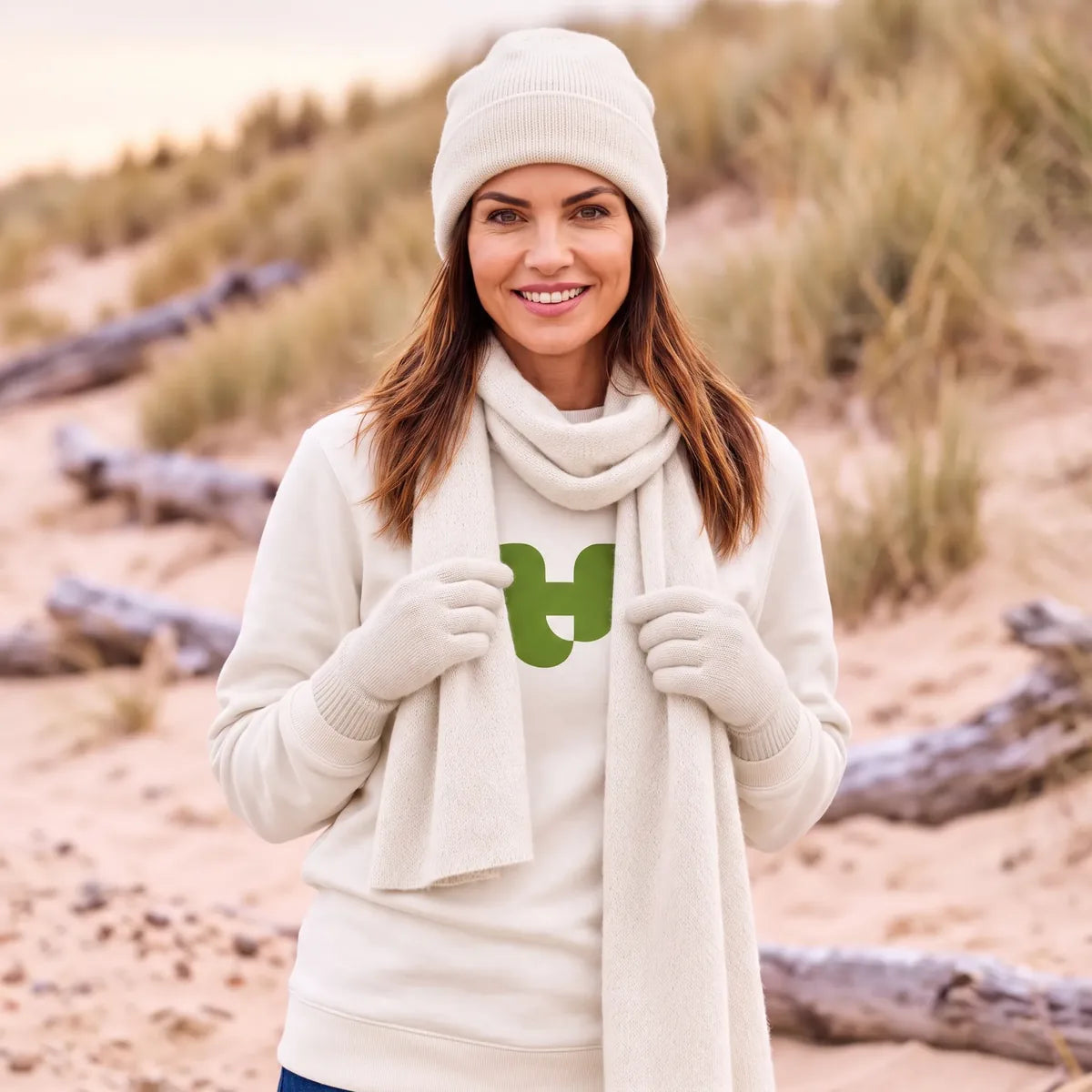 Femme souriante portant l'écharpe en cachemire blanc cassé avec le bonnet et les gants assortis, dans les dunes