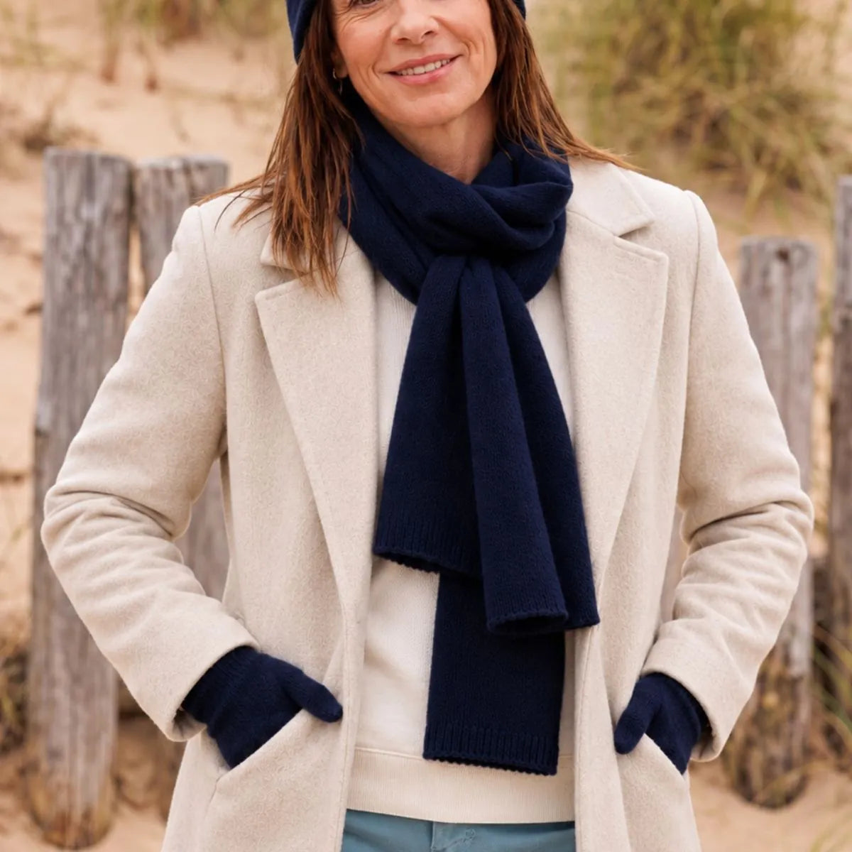 Femme en manteau crème portant l'écharpe en cachemire bleu marine nouée et les gants assortis