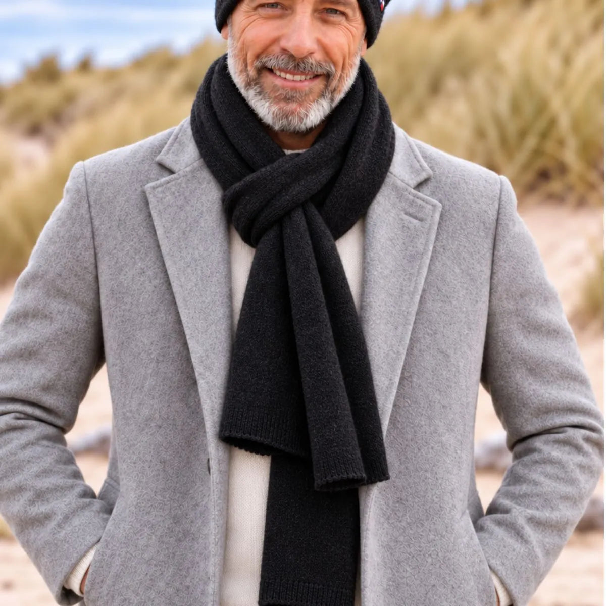 Homme en manteau gris portant l'écharpe en cachemire noire nouée sur un pull crème