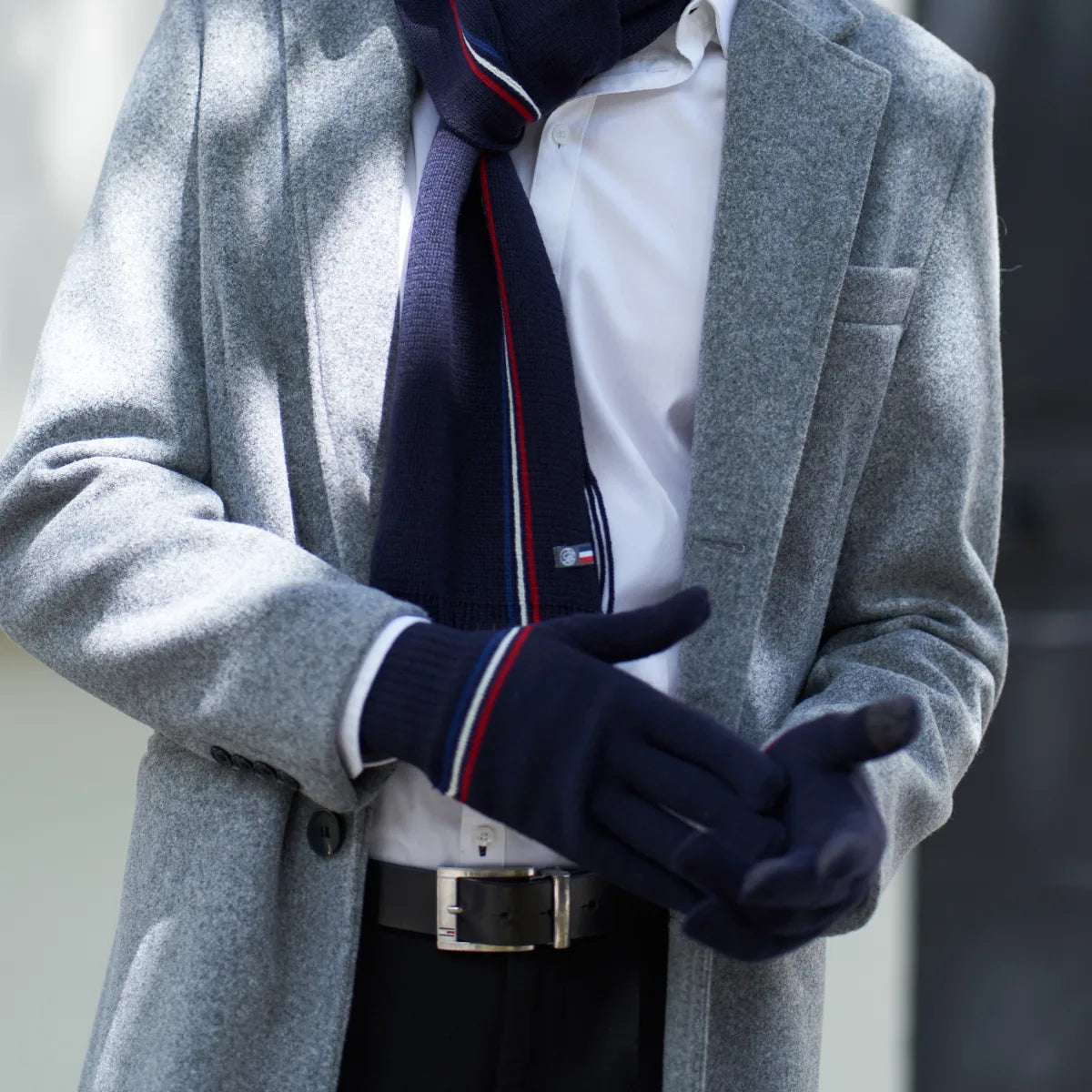 Gants d'hiver homme bleu marine tactiles portés avec un manteau gris et une écharpe bleu marine à rayures tricolores