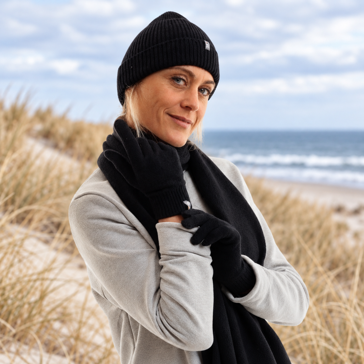gants noir en lain emerinos porté par une femme avec des dunes de sables derrière